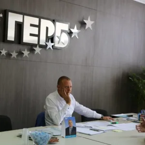 Двама мъже разговарят в офис на ГЕРБ, на фона на партийното лого